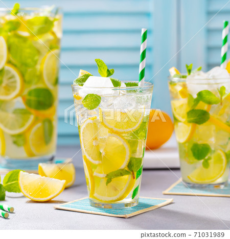 Lemonade, lemon, mint cocktail in glasses and jug. Blue background. Close up. 71031989