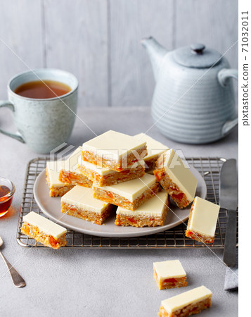 Oat, coconut, apricot bars and white chocolate with cup of tea. Grey background. 71032011