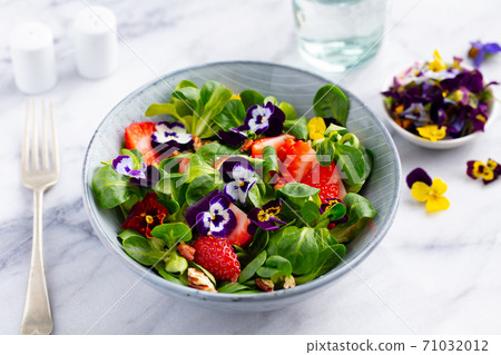 Fresh green salad with strawberries and edible flowers in a bowl. Marble background. Close up. 71032012