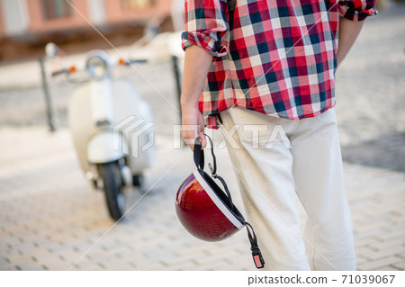 Man preparing to ride his scooter and holding a helmet 71039067