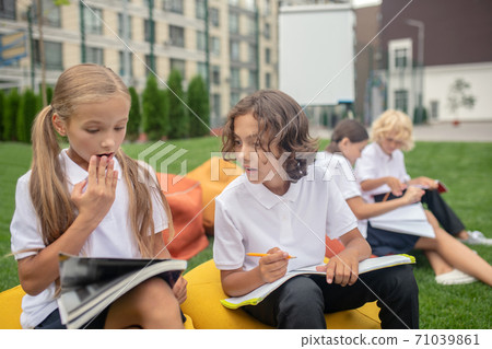 Dark-haired schoolboy in white shirt peeping to his classmates notebook Dark-haired schoolboy in white shirt peeping to his classmates notebook 71039861