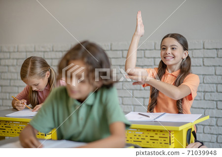 Dark-haired girl raising her hand ready to answer 71039948