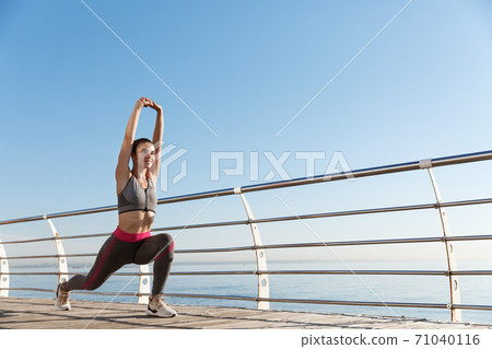 Low angle shot of healthy attractive fitness woman stretching legs and hands, workout alone near the sea. Girl warming-up before run 71040116