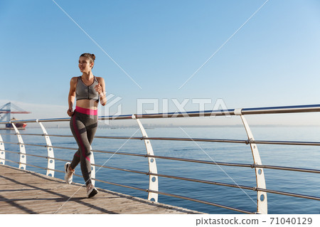 Portrait of healthy attractive fitness woman running near the sea. Girl jogging and smiling outdoors Portrait of healthy attractive fitness woman running near the sea. Girl jogging and smiling outdoors 71040129