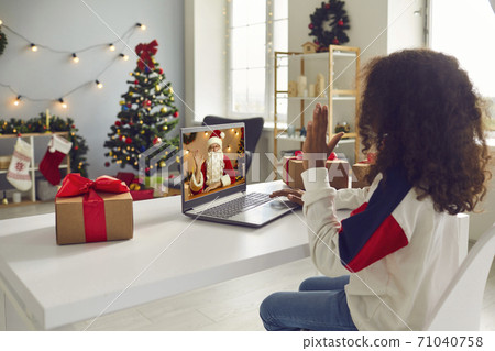 Little African-American girl having video calling old Father Christmas sitting at desk at home 71040758