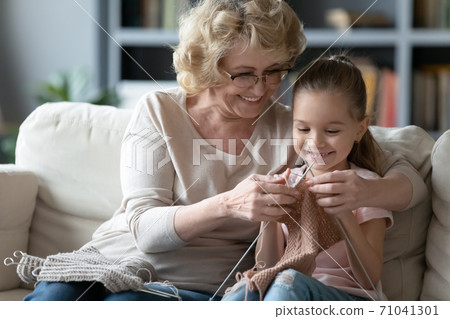 Happy proud elderly retired grandmother teaching little granddaughter creating clothing. Happy proud elderly retired grandmother teaching little granddaughter creating clothing. 71041301