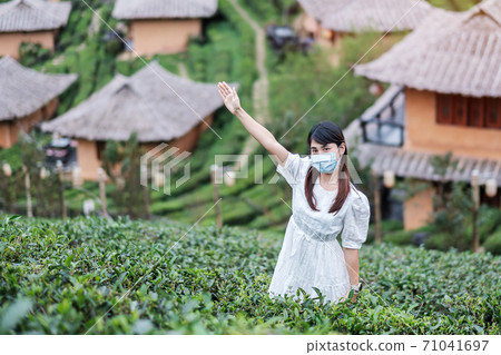 Happy tourist woman wearing surgical face mask  enjoy beautiful Tea garden, protection Coronavirus disease (Covid-19) infection. New Normal, travel, vacation and holiday concept 71041697