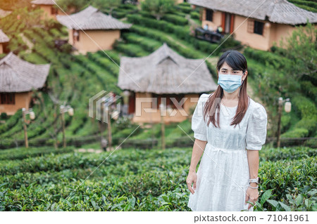 Happy tourist woman wearing surgical face mask  enjoy beautiful Tea garden, protection Coronavirus disease (Covid-19) infection. New Normal, travel, vacation and holiday concept 71041961