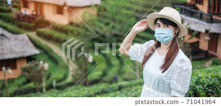 Happy tourist woman wearing surgical face mask enjoy beautiful Tea garden, protection Coronavirus disease (Covid-19) infection. New Normal, travel, vacation and holiday concept Happy tourist woman wearing surgical face mask enjoy beautiful Tea garden, protection Coronavirus disease (Covid-19) infection. New Normal, travel, vacation and holiday concept 71041964