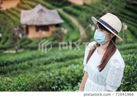 Happy tourist woman wearing surgical face mask enjoy beautiful Tea garden, protection Coronavirus disease (Covid-19) infection. New Normal, travel, vacation and holiday concept Happy tourist woman wearing surgical face mask enjoy beautiful Tea garden, protection Coronavirus disease (Covid-19) infection. New Normal, travel, vacation and holiday concept 71041966