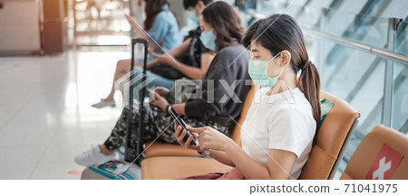 Young female wearing face mask and using mobile smartphone in airport, protection Coronavirus disease (Covid-19) infection, Asian woman traveler sitting on chair. New Normal and social distancing Young female wearing face mask and using mobile smartphone in airport, protection Coronavirus disease (Covid-19) infection, Asian woman traveler sitting on chair. New Normal and social distancing 71041975