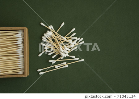 Eco-friendly cotton swabs. A cardboard box containing recyclable bamboo cotton buds on a green surface. Zero waste concept. Eco product. Cosmetic sticks in a box. Wooden sticks for cleaning ears. 71043134