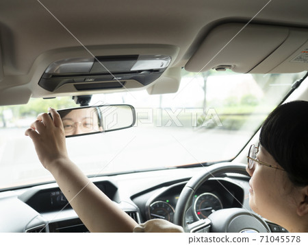 A young woman adjusting the rearview mirror before driving 71045578