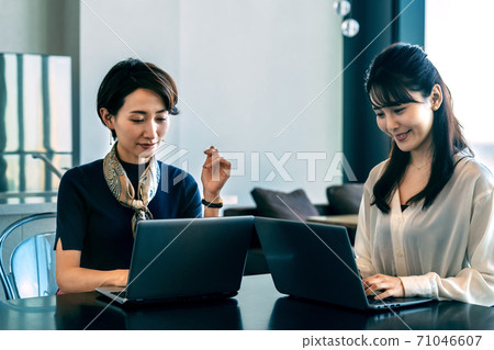 Two business women (casual) meeting while operating a computer in the office 71046607