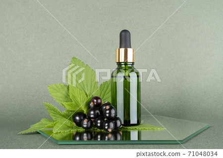 One green glass bottles with serum, essential oil or other cosmetic product with sprig of black currant on mirror, green background. Natural Organic Beauty Cosmetic concept. Front view 71048034