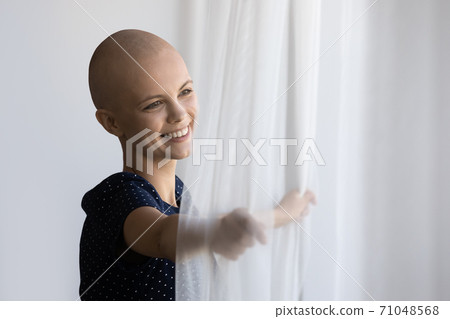 Close up smiling dreamy hairless woman opening curtains in morning 71048568