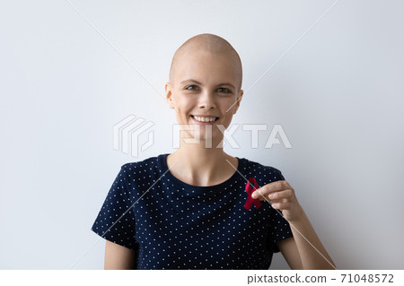Head shot portrait smiling hairless woman holding awareness red ribbon Head shot portrait smiling hairless woman holding awareness red ribbon 71048572