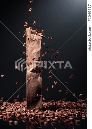 Large piece of dark chocolate and falling chocolate crumbs. 71049517