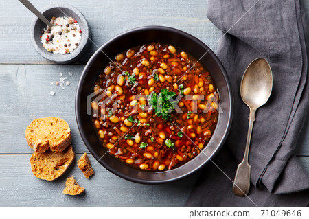 Bean soup in a black bowl. Grey wooden background. Close up. Top view. 71049646