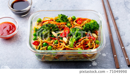 Stir fry noodles, udon with vegetables in lunch box. Grey background. Close up. Stir fry noodles, udon with vegetables in lunch box. Grey background. Close up. 71049998
