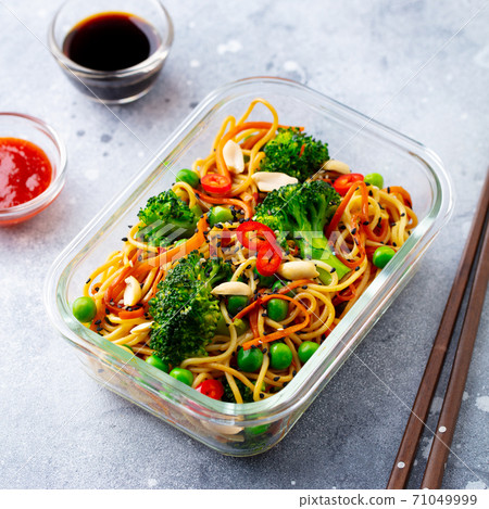 Stir fry noodles, udon with vegetables in lunch box. Grey background. Close up. Stir fry noodles, udon with vegetables in lunch box. Grey background. Close up. 71049999