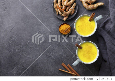 Turmeric drink, latte, tea, milk with cinnamon in a mug with fresh and powder turmeric. Dark background. Copy space. Top view. 71050505