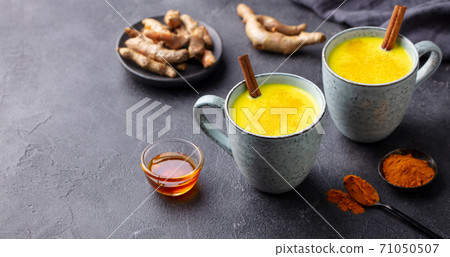 Turmeric drink, latte, tea, milk with cinnamon in a mug with fresh and powder turmeric. Grey background. Copy space. 71050507