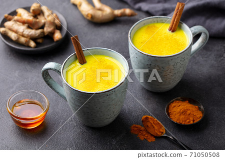 Turmeric drink, latte, tea, milk with cinnamon in a mug with fresh and powder turmeric. Grey background. Close up. 71050508