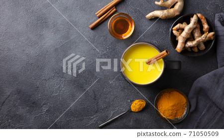 Turmeric drink, latte, tea, milk with cinnamon in a mug with fresh and powder turmeric. Dark background. Copy space. Top view. 71050509