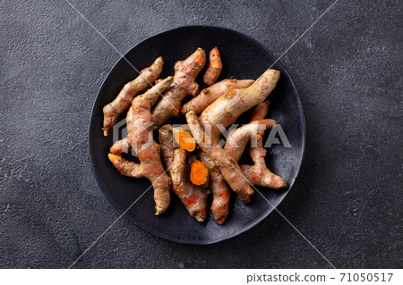 Fresh turmeric, curcumin, tumeric roots on a black plate. Superfood product. Dark background. Close up. Top view. 71050517