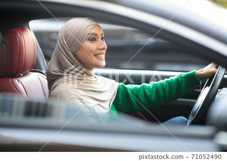 Smiling muslim woman driving her new car in urban city Smiling muslim woman driving her new car in urban city 71052490