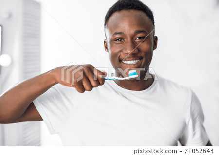 Happy African American Man Cleaning Teeth Standing In Bathroom Happy African American Man Cleaning Teeth Standing In Bathroom 71052643