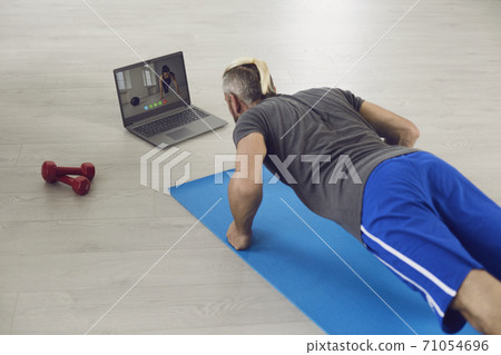 Exercise at home online. Girl doing exercises on the floor watching a video course using a laptop in a living room at home. Exercise at home online. Girl doing exercises on the floor watching a video course using a laptop in a living room at home. 71054696