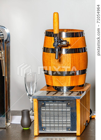 Keg of wine and the stainless steel crane on it. A wine glass in the background. 71054964