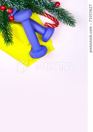 Christmas fitness. Healthy and active lifestyles greeting card concept. Purple dumbbells, yellow rubber band, candy and fir-tree on pink 71055627