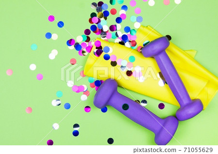 Christmas fitness. Healthy and active lifestyles greeting card concept. Purple dumbbells, yellow rubber band and colorful confetti 71055629