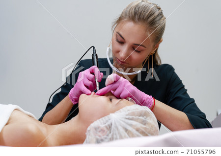 Cosmetology cabinet client lies on couch. Beautician applies marking on eyebrows. Cosmetology cabinet client lies on couch. Beautician applies marking on eyebrows. 71055796