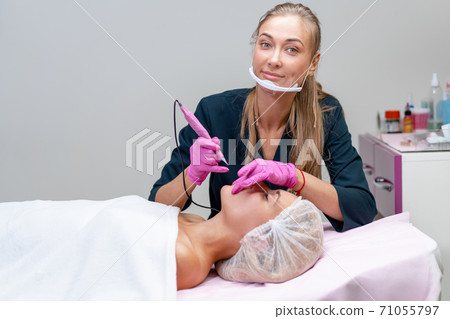 Cosmetology cabinet client lies on couch. Beautician applies marking on eyebrows. 71055797