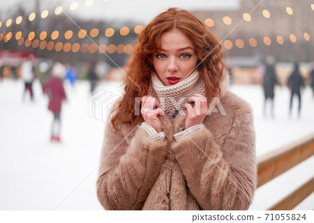 Young beautiful redhead girl freckles ice rink on background. Pretty woman curly hair portrait walking on new year fair Young beautiful redhead girl freckles ice rink on background. Pretty woman curly hair portrait walking on new year fair 71055824