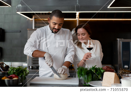 Handsome young African chef is cooking together with his Caucasian girlfriend in the kitchen using red wine as an ingredient. 71055870