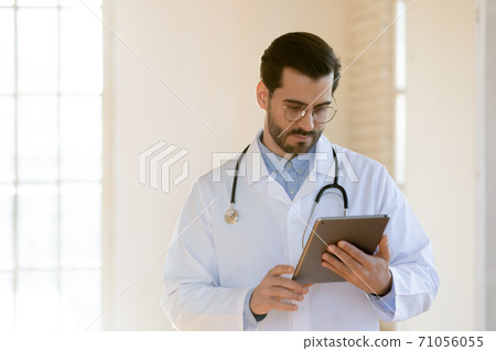 Pensive millennial doctor focused on tablet screen counseling patient online 71056055