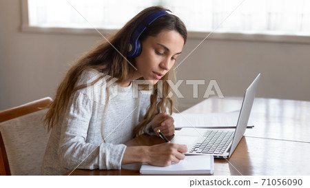 Female student sitting by laptop in earphones listening distant lecture Female student sitting by laptop in earphones listening distant lecture 71056090