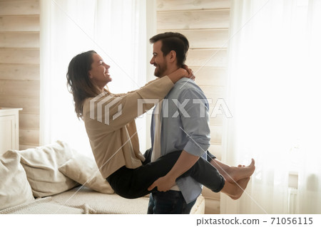 Affectionate boyfriend holds smiling girlfriend in arms lifting in air 71056115