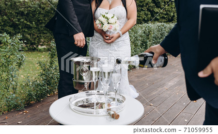 Wedding registrar fill glasses with champagne for happy bridal couple. Wedding registrar fill glasses with champagne for happy bridal couple. 71059955