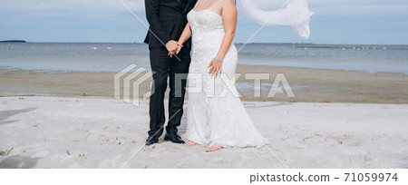 Wedding couple dancing at the beach, young bride wears white dress and long veil. 71059974