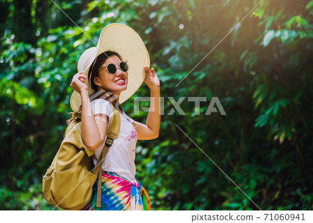 Young girl with backpack enjoying  travel nature in the forest Lush green trees. Happy smiling woman With nature travel, rural forest. In the summer, Travel relax, Travel Thailand. 71060941