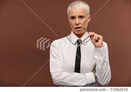 Masculine female in white shirt and black necktie holding eyeglasses by mouth 71062630