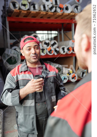 Happy warehouse worker having coffee at break while consulting with colleague Happy warehouse worker having coffee at break while consulting with colleague 71062652