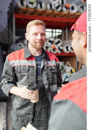 Young male worker in uniform having coffee during conversation with colleague Young male worker in uniform having coffee during conversation with colleague 71062654
