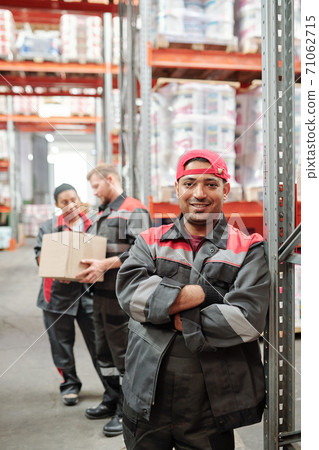Happy young Latino worker in grey uniform and gloves crossing arms by chest 71062715